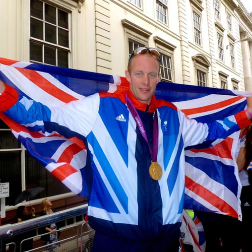 David Smith MBE holds a British flag up behind him with arms spread wide