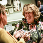 Professor Pat Price at the 9th World Cancer Series. Professor Price smiles while talking with a colleague. She wears a smart pink and black dress and has bobbed fair hair.