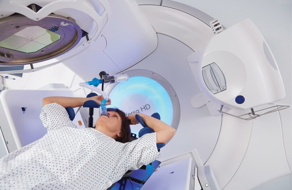 A patient with arms overhead, is treated with a linear accelerator, a large machine that gives out targeted radiation to the tumour site