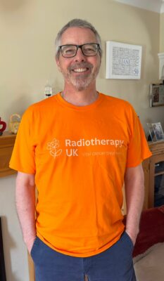 Andy smiles at the camera, wearing his bright orange Radiotherapy UK T-shirt