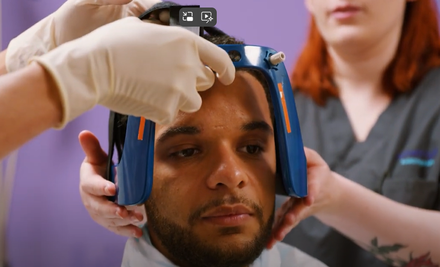 The treatment team lift a blue head frame onto the patient's head and begin to attach it.