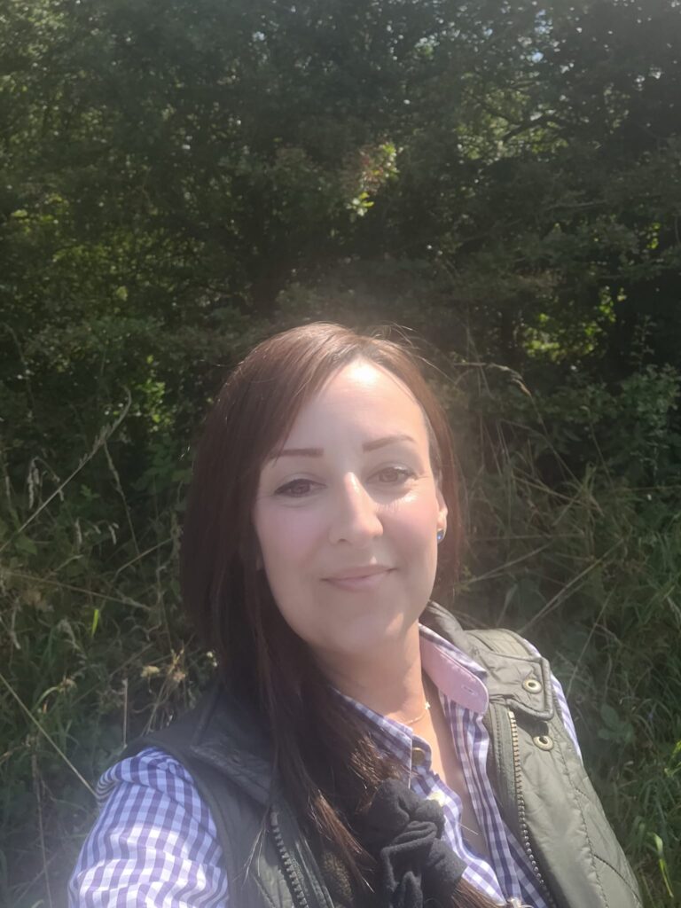 Kelly Watson, 43 from Yorkshire. Kelly has long brown hair and smiles at the camera. She is outside on a sunny day.