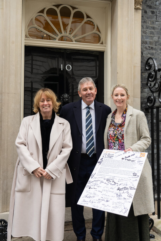 Professor Price, Bryan Robson OBE and Sarah Quinlan MBE outside No10 Downing Street holding the letter from MPs covered in signatures