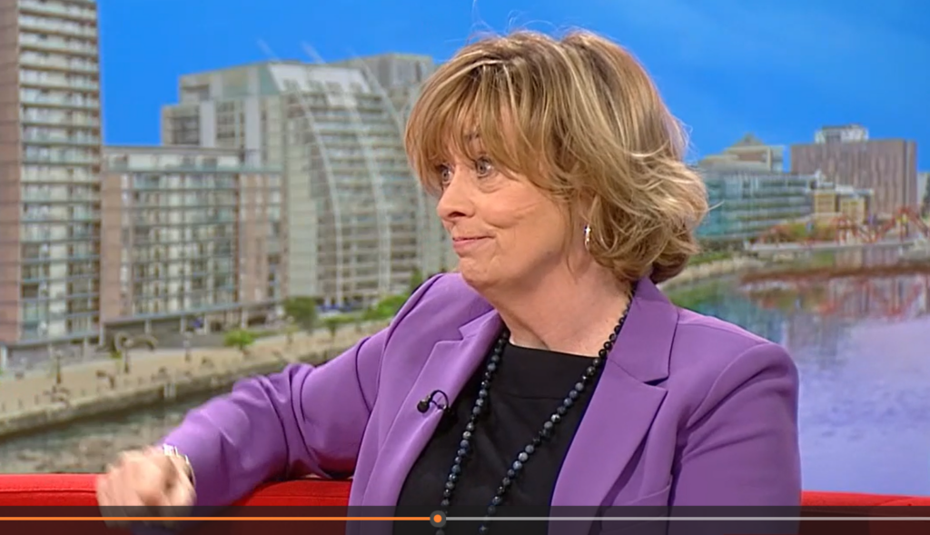 Professor Pat Price on BBc Breakfast, in a purple jacket and black top, with bobbed highlighted hair.