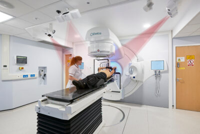 A radiotherapy professional positions a patient carefully on a radiotherapy machine. This is like a horizontal bed for the patient to lie on while a large structure moves around them, delivering a careful dose of radiation
