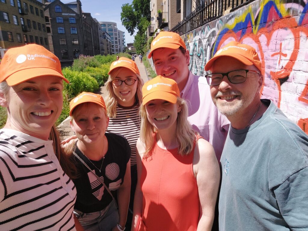 Radiotherapy UK team outside in the sunshone wearing orange caps and smiling
